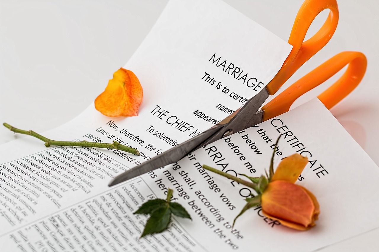 Orange scissors cutting through a marriage certificate with dried rose petals, symbolizing divorce and the end of a marriage.